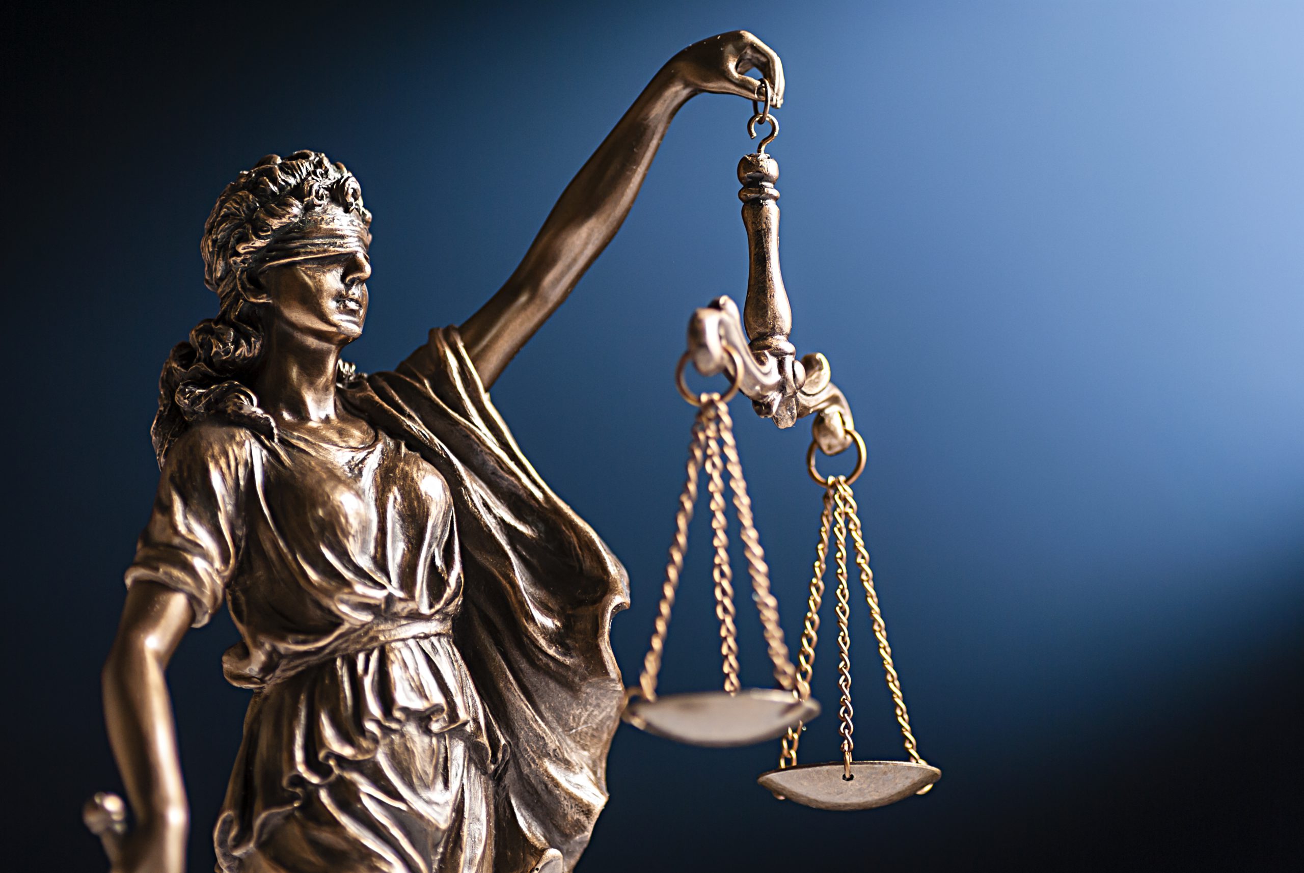 Bronze Lady Justice statue holding the scales of justice against a dark blue background